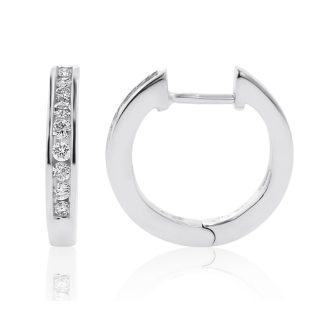 These delicate earrings feature round channel-set diamonds totaling 1/4 carat weight, uniquely crafted into chic, huggie-style hoops. Made from 10 karat white gold, their timeless design exudes a combination of modern sophistication and classic elegance. These exquisite hoops hug close to the ear for a minimalistic yet dazzling look.